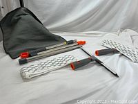 Photo showing the whole set including the mesh carry bag, extendable handle, squeegee, scrubber, and microfiber pads arranged on a white surface