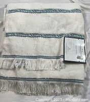 Two white bath towels folded, showing blue stripe detail and fringe edges with attached label