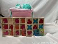 Pink plastic container with assorted sand and beach toys and three wooden Tic Tac Toe games arranged in front