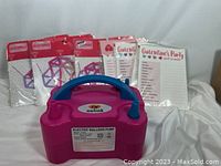 Full view of pink and blue Nulink electric balloon pump with party banners and party sheets in background