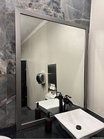 Full view of one large commercial mirror mounted on a wall above a sink, showing a modern bathroom environment and a framed reflective surface.