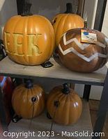 Four orange lighted pumpkins and one brown decorative pumpkin on shelf, showing various designs including 'EEK' and chevron pattern.