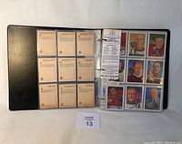 Open black binder showing protective sleeves with illustrated hockey player cards and informational inserts related to the Hockey Hall of Fame series