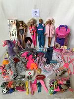 Wide view showing four dolls, pink Barbie horse, Barbie clothing, shoes, hair accessories, and pink storage container.