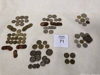 Overview photo showing multiple groups of international coins arranged in stacks and rows on a white surface with a lot card marked 71 visible.