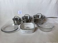 Front view of three KitchenAid stainless steel saucepans with lids, two glass pie plates/baking dishes, and one vintage Corningware baking dish with Country Cornflower pattern.