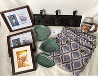 Photo showing entire lot items on white background: 2 curtain panels, 3 photo frames with vintage style prints, 3 green leaf pottery vessels, ceramic Toby jug style mug, dark wood coat hook with ornate black metal hooks