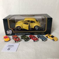Front view of boxed yellow Volkswagen Beetle 1:18 diecast model with six small diecast cars lined up in front.