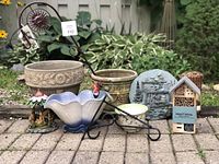 Photo showing all garden items including pots, decorative hooks, insect hotel, and garden decor on brick patio with plants in background