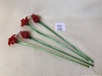 Four red blown glass flowers with long green stems arranged on a flat surface