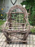 Front view of large rustic twig chair showing overall shape, armrests, curved twig design in front and vertical twig backrest slats.