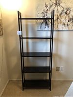 Front view of the IKEA Laiva black-brown shelving unit showing all five shelves and the slim frame design against a wall with floral art.