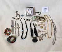 Photo displaying a variety of costume jewelry pieces and watches laid out on a light surface. Shows watches, beaded bracelets, bangle bracelets, rings, earrings, and necklaces.