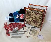 Full collection of knitting supplies arranged including vintage Eatons bag, knitting needles, yarn and patterns on white background.