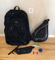 Full lot showing large MEC backpack with front zip-off smaller backpack, Reebok one-shoulder backpack, money belt, tissue roll, blue cup, and Canadian flag patch.