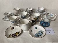 Photo showing all teacups, saucers, and creamers from the lot arranged on a flat surface, showing variety of floral patterns and sizes including the Royal Albert Blue Blossom teacup and 2 creamers (ceramic and stainless steel).