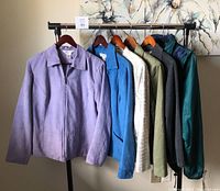 Front view of six lightweight women's jackets hanging on rack: lavender, blue, cream, olive green, dark gray, teal