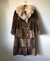 Full view of women's vintage fur coat hanging on wooden hanger showing brown fur body and large white fur collar.
