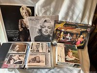 Photo showing Marilyn Monroe calendar in binder alongside two puzzles and two trading card boxes.