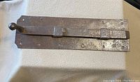Top-down view of the large iron barn door sliding bolt latch showing the rounded handle, rectangular base plate with rivets, and aged rusty finish.