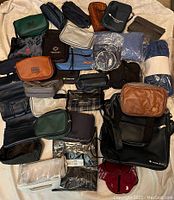 Top-down view of a large assortment of various travel bags in multiple colors, showing a wide mix of pouches, vanity bags, and cosmetic bags spread out on a white surface.