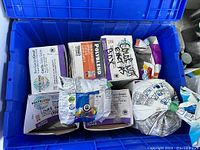 Box containing multiple bags and boxes of tile grout in different colors, inside a blue plastic container.