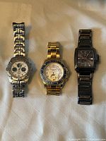 Front view of three men's watches on fabric surface showing faces and metal bands