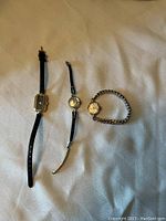Photo showing all three vintage ladies wrist watches side by side on a cloth surface, with varying bands including leather and metal elastic.