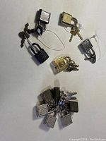 Photo showing 11 luggage locks in silver and gold tones, each with keys attached by wire or rings.