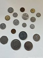 Top view of coin collection laid out on white surface showing variety of sizes and shapes including round and polygonal coins.