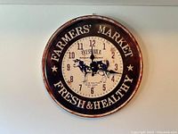Full frontal view of round metal clock with Farmers' Market design and cow illustration.
