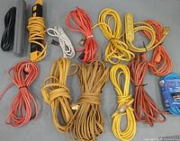 Photo of various outdoor electrical cords of different lengths and colors including black, yellow, orange, white, red, and blue cords, some with multi-outlet end caps.