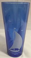 Photo of cobalt blue glass cocktail shaker with etched white sailboat, birds, and waves design, showing front profile and clarity of glass.
