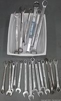 20 metal open ended and combination wrenches in a plastic container and arranged on black surface.