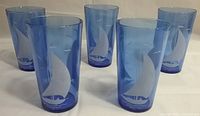 Photo of five cobalt blue Depression glass ice tea glasses, each featuring an etched sailboat design, arranged in a group on a flat surface.