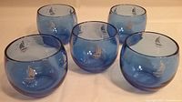 Photo showing five cobalt blue glass roly poly tumblers with a sailboat motif from the 1930s, arranged in a group.