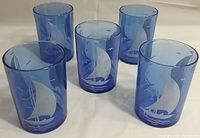 Five cobalt blue Hazel Atlas water glasses from the 1930s with sailboat design arranged on white surface