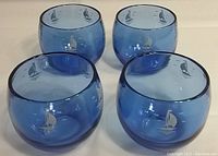 Photo showing four cobalt blue roly poly tumblers with sailboat decoration from the 1930s Hazel Atlas Depression glass collection.