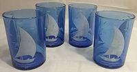 Four cobalt blue Hazel Atlas Depression glass water glasses with sailboat etchings arranged in a group on a white surface.