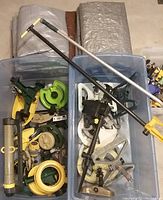 View of two large plastic tubs filled with various garden sprinklers and four folded tarps stacked behind them.