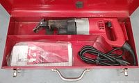 Red Milwaukee heavy duty reciprocating saw inside open red metal carrying case with paper manual and attached power cord coiled in the case.