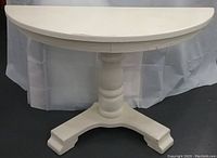 Front view of white painted oak half-round hall table with pedestal base against plain backdrop.