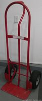 Front view photo of red metal hand truck showing frame, handle, bottom plate, and two large black tires.