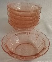 Stack of six pink Depression glass side bowls with one bowl placed in front, showing the Cherry Blossom pattern and scalloped rim.