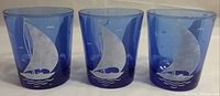 Three cobalt blue old fashioned glasses with etched sailboat design, front view showing the detailed sailboat and wave pattern on each glass.