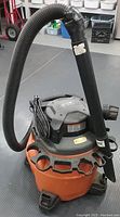 Image of orange and black 14 gallon Rigid shop vacuum with hose attached upright on floor.