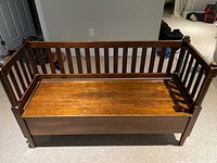 Full front view of wooden bench showing slatted back and arm rails with rounded post finials.
