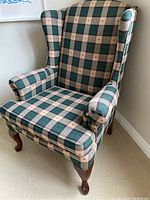 Side angle view of wingback chair showing tartan fabric and wooden legs with scratches