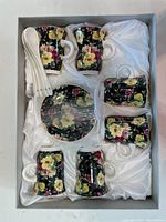Top view of the set in the box showing 6 coffee cups, 6 saucers, and 6 spoons arranged neatly on a satin liner.