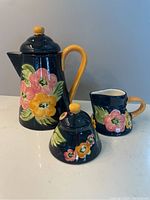Photo of the full set showing the coffee pot, milk pitcher, and sugar pot from the front with floral design